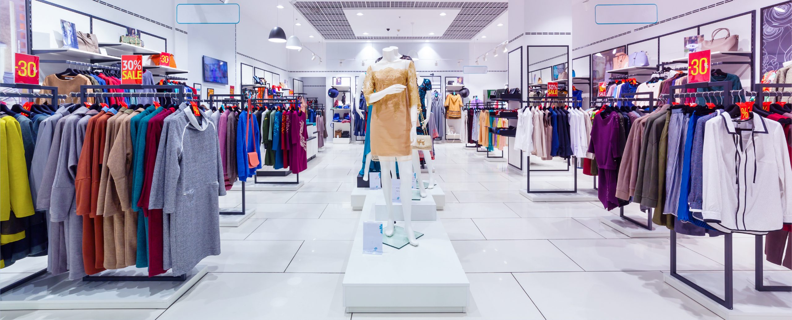 A spacious clothing store interior with neatly arranged racks of colorful clothing and central display stands showcasing mannequins dressed in trendy outfits, under bright lighting.