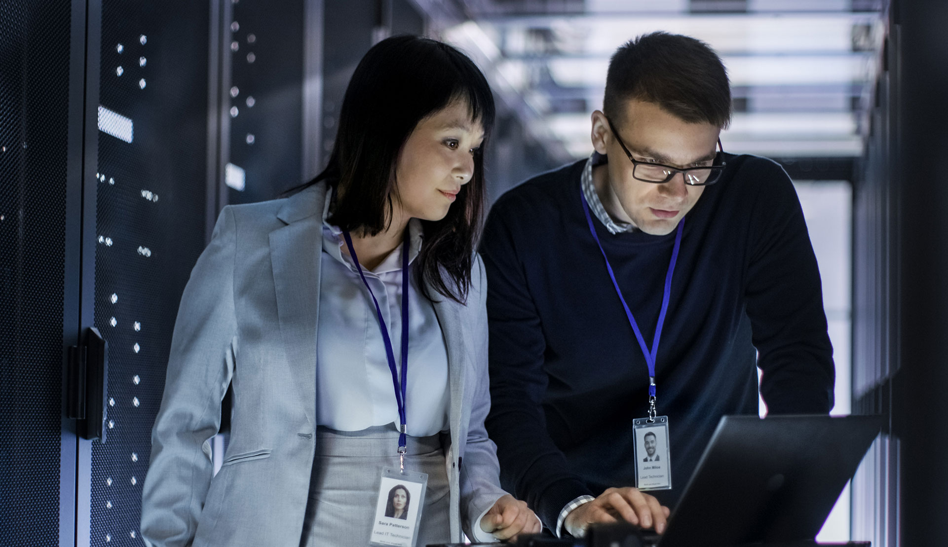 Two IT professionals examining a laptop screen in a server room.