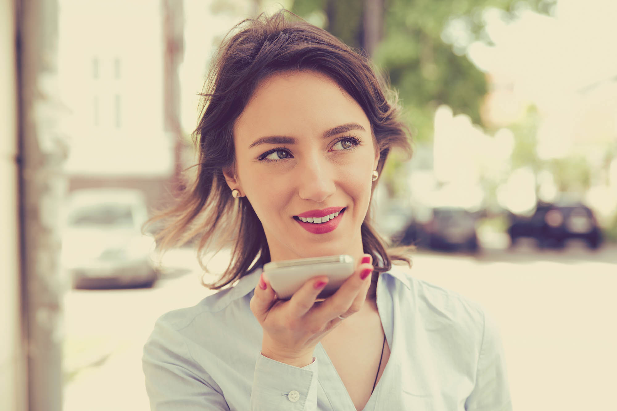 Woman speaking into a smartphone on a city street, with a smile on her face.