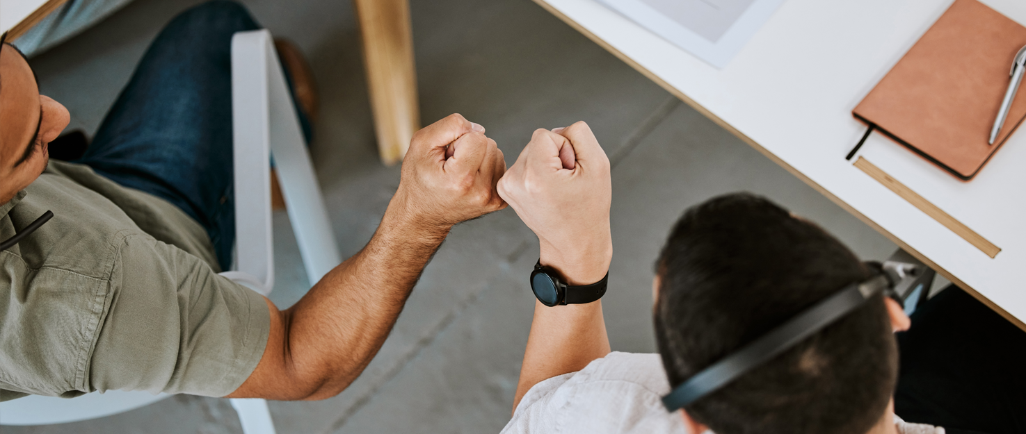 Two colleagues giving a fist bump over a workspace in a collaborative office environment.