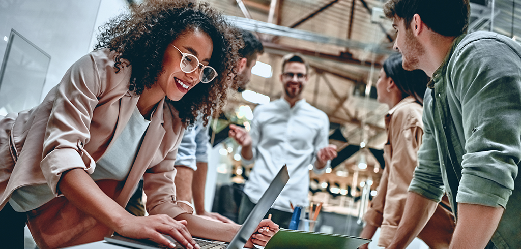 A dynamic office setting with a group of young professionals engaging around a laptop in a creative brainstorming session.