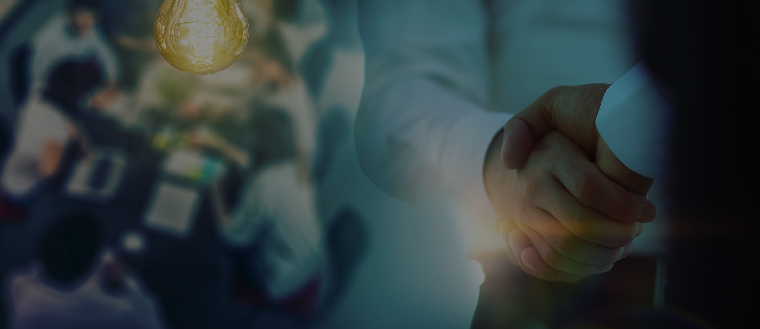 A close-up of two people shaking hands in a dimly lit room, with a glowing light bulb representing an idea above them.